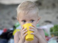 Niño de pie en la playa y sosteniendo taza de plástico - foto de stock