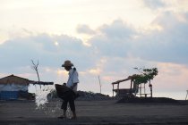 Productor de sal salpicando agua en la arena, bali, indonesia - foto de stock