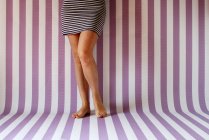Imagen recortada de piernas de mujer contra fondo rayado - foto de stock