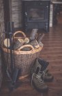 Boots next to a basket filled with firewood and hearth set — Stock Photo