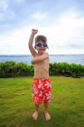 Boy wearing swimming trunks and goggles standing at meadow with sea on background — Stock Photo