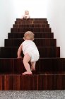 Back view of Baby boy climbing on wooden stairs, sister sitting at top — Stock Photo