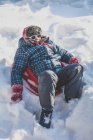 Junge sitzt im Winter auf Schlitten im Schnee — Stockfoto
