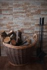 Firewood em uma cesta ao lado de um conjunto de lareira — Fotografia de Stock
