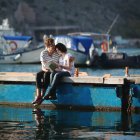 Beautiful teenage couple sitting on jetty embracing — Stock Photo