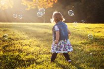 Girl surrounded by soap bubbles in park — Stock Photo