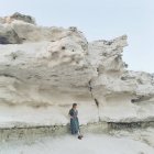 Mulher vestindo vestido encostado às rochas e olhando para a vista — Fotografia de Stock