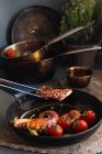 Крупный план Жареный осьминог с помидорами и каперсами на черной сковороде — стоковое фото