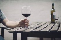 Image recadrée de l'homme tenant un verre de vin rouge sur une table en bois à l'extérieur — Photo de stock