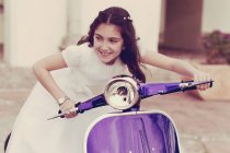 Girl wearing first communion dress playing on a scooter — Stock Photo