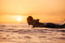 Gros plan d'un surfeur souriant pagayant pour attraper une vague au coucher du soleil, San Diego, Californie, Amérique, États-Unis — Photo de stock