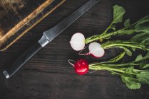 Radishes with a knife and chopping board on a wooden table, top view — Stock Photo