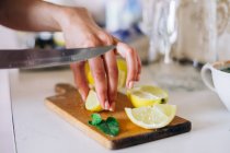 Женская рука режет лимон на деревянной тарелке на столе — стоковое фото