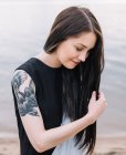 Портрет женщины с татуировкой, держащей длинные волосы — стоковое фото