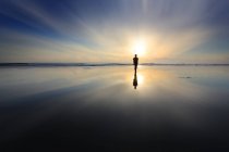Silhueta de menino andando na praia ao pôr do sol — Fotografia de Stock