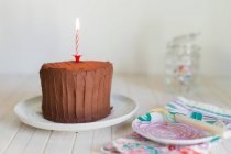 Chocolate Birthday cake with candle on plate over wooden background — Stock Photo
