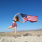 Woman doing tree pose in desert and holding american flag, Nevada, America, USA — Stock Photo