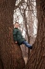 Портрет мальчика в теплой куртке, взбирающегося на дерево — стоковое фото