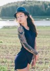 Hipster Mujer con manga de tatuaje de pie en el paisaje rural - foto de stock