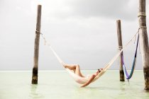 Женщина в солнечных очках отдыхает в гамаке над морем — стоковое фото