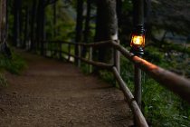 Lâmpada de óleo iluminada na cerca ao longo do caminho da floresta — Fotografia de Stock