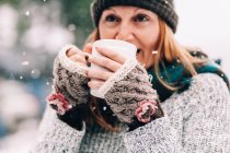 Frau steht im Schnee und hält Heißgetränk — Stockfoto