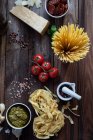 Pasta, pesto, ajo, tomates y parmesano en la mesa, vista superior - foto de stock