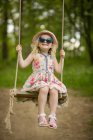Дівчина в сонцезахисних окулярах сидить на гойдалці — стокове фото