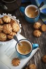 Печиво, книга і чашки кави над дерев'яним столом — стокове фото