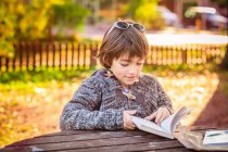 Boy reading book at wooden table in park — Stock Photo