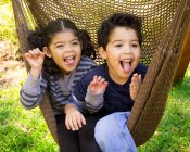 Hermano gemelo y hermana sentados en hamaca y tirando caras divertidas - foto de stock