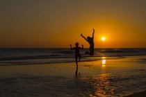 Silhouette von Jungen und Mädchen, die am Strand springen — Stockfoto