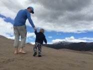 Padre e hijo caminando en las montañas bajo el cielo nublado - foto de stock