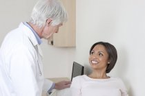 Médico hablando con paciente femenina en sala de examen - foto de stock