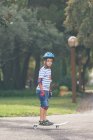 Boy standing on skateboard in park and looking at camera — Stock Photo