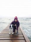 Девушка с собакой стоит на пирсе у моря — стоковое фото