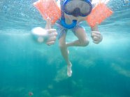 Niño con snorkel, máscara y alas de agua mostrando pulgares en el océano - foto de stock