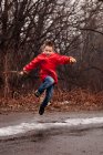 Menino vestindo casaco vermelho pulando na rua no inverno — Fotografia de Stock