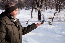 Hombre alimentando aves en bosque de invierno - foto de stock