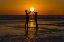 Side view of young friends holding sun on beach at sunset — Stock Photo