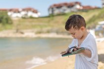 Крупним планом хлопчик стоїть на пляжі і чистить пісок від фліп-флоп — стокове фото