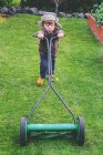 Menino usando chapéu cortando gramado no jardim — Fotografia de Stock