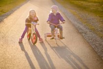 Dos monas hermanas felices montando bicicletas juntas - foto de stock