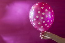 Mão segurando balão rosa com bolinhas brancas — Fotografia de Stock