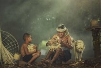 Дід навчає онука робити плетений рибальський кошик біля великого білого собаки — стокове фото