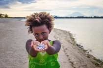 Ragazza in piedi sulla spiaggia e mostrando conchiglie, Indonesia — Foto stock