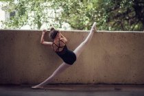 Visão traseira da linda menina bailarina segurando parede e alongamento — Fotografia de Stock