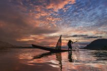 Hombre de pie en barco de pesca al atardecer, río Mekong, Tailandia - foto de stock