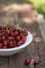 Bowl of cherries on wooden table, blurred background — Stock Photo