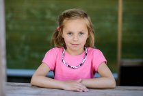 Retrato de uma menina loira sorridente sentada à mesa — Fotografia de Stock
